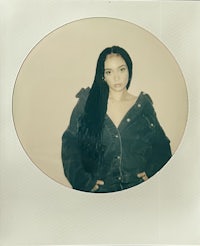 a woman in a black jacket is posing in front of a polaroid