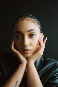 a woman in a black leather jacket posing with her hands on her face